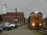 Under threatening skies, a westbound empty hopper passes the Amtrak station